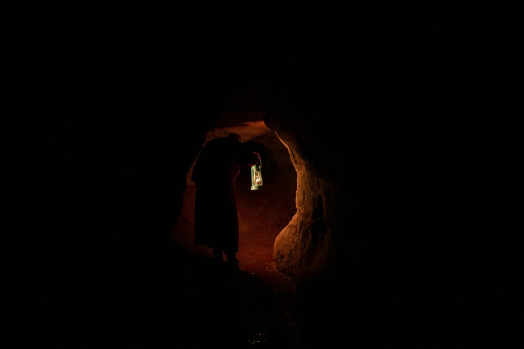 Silhouette of a person holding a lantern in a dark cave, creating a mysterious ambiance.